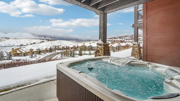 Un jacuzzi en un balcón con vistas a un paisaje nevado y casas.