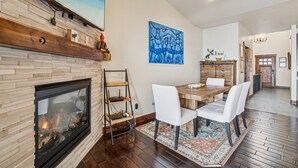 Un comedor con una mesa de madera y sillas blancas, una chimenea de piedra y un cuadro en la pared.
