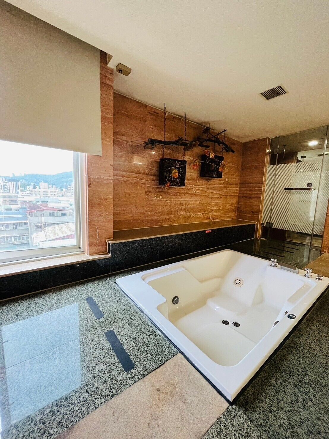 A modern bathroom with a large bathtub, a window with a city view, and a wooden wall with decorative elements.