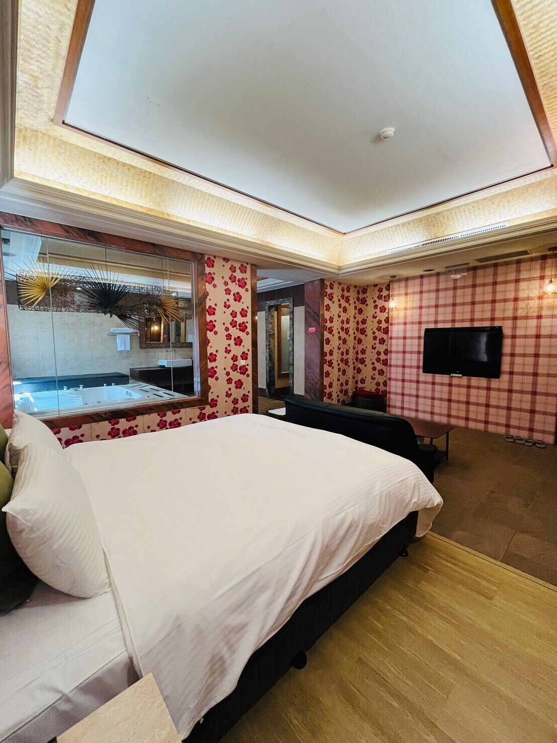 Una habitación de hotel moderna con una cama grande, un área de descanso, un televisor de pantalla plana y vista a una piscina a través de un muro de cristal.