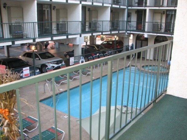 Un hotel con zona de piscina, varios balcones y aparcamiento con coches.