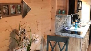 Een houten blokhut van binnen met een keukenhoek, een eettafel met een vaas witte bloemen en een blauwe stoel.