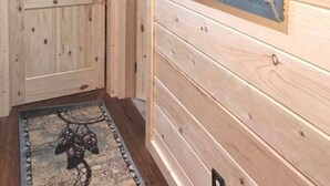 Een houten gang met een schilderij van paarden in een lijst aan de muur, een deur en een vloerkleed met een patroon.