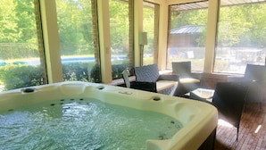 Un jacuzzi en una habitación con ventanas amplias, mobiliario exterior y vistas a zonas verdes.