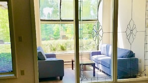 Una sala de estar moderna con un sofá y una mesa de centro, ventanas amplias con vistas a zonas verdes y un separador decorativo de metal.