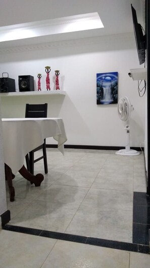 A room with a white table, a white fan, and a painting on the wall. - Harold's place 201 (San Andrés)
