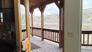 Une porte en bois ouverte donne sur une terrasse extérieure couverte, d’où l’on peut admirer un paysage vallonné.