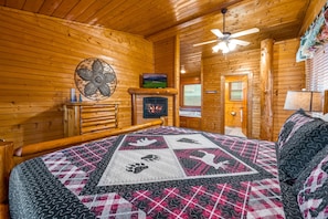 A log cabin room with a bed, a fireplace, a television, and a ceiling fan. - PRIME Location,WIFI, Smart TV, Pet WLCM,Game Rm,HDTV,HotTub,7mints to City,COZY  (Gatlinburg)
