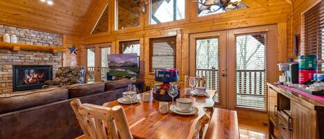 A wooden cabin interior with a fireplace, dining table, and seating area.
