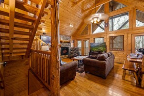 A log cabin interior with a fireplace, wooden furniture, and large windows. - PRIME Location,WIFI, Smart TV, Pet WLCM,Game Rm,HDTV,HotTub,7mints to City,COZY  (Gatlinburg)