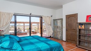 A bedroom with a large bed, a wooden wardrobe, and a sliding glass door leading to an outdoor patio with a view of the landscape. - Fabulous Fall and Winter:  HEATED POOL! (Todos Santos)