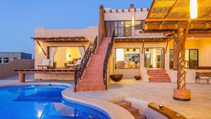 A poolside area with a clear blue pool, a staircase leading to a covered patio, and a lounge area with seating. - Fabulous Fall and Winter:  HEATED POOL! (Todos Santos)