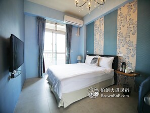 A hotel room with a large bed, a flat-screen TV, a bedside table with a lamp, and a window with curtains. - Brown B&B (Chishang)