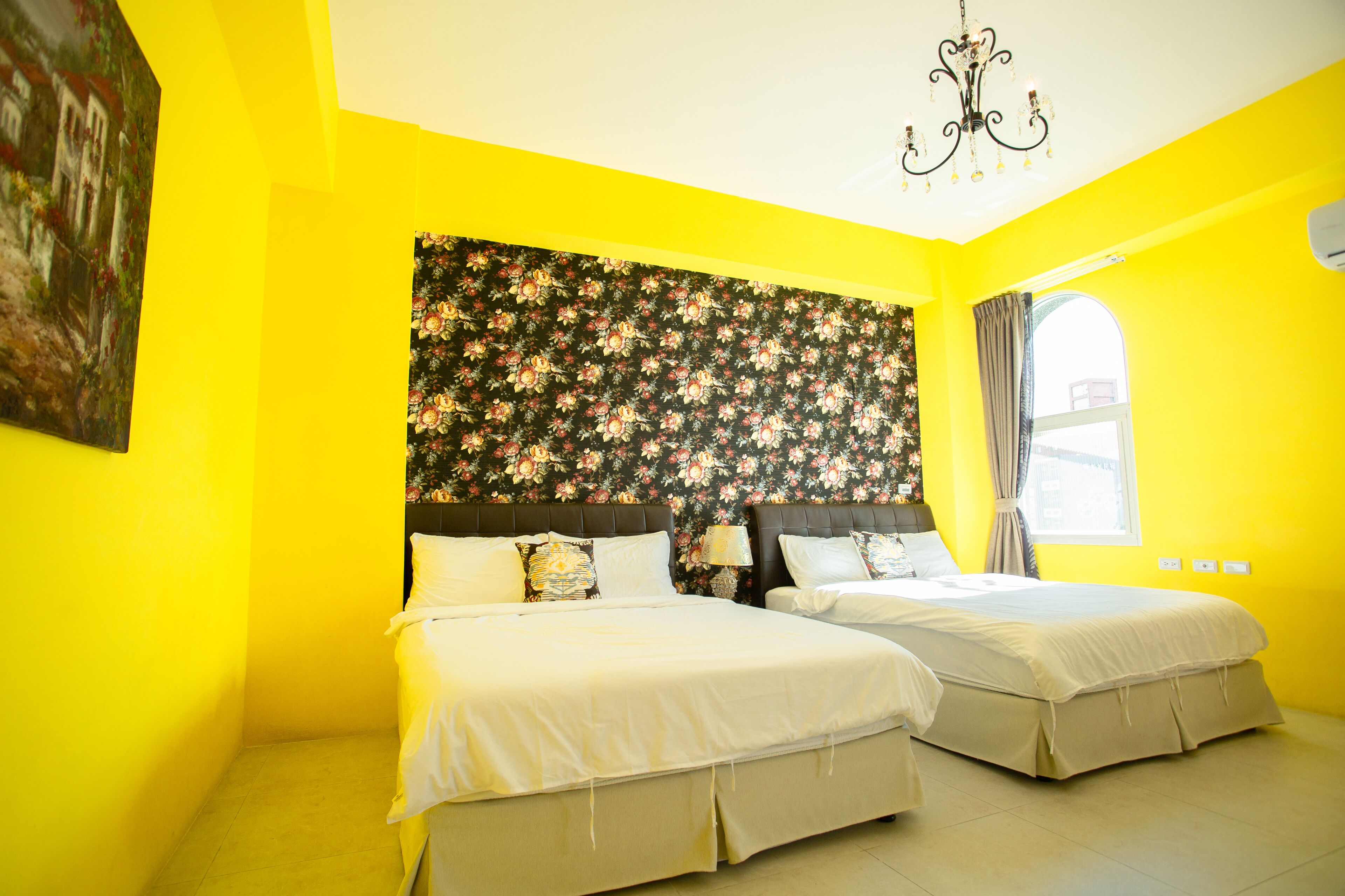 A bright yellow room with two beds, a floral headboard, and a chandelier.