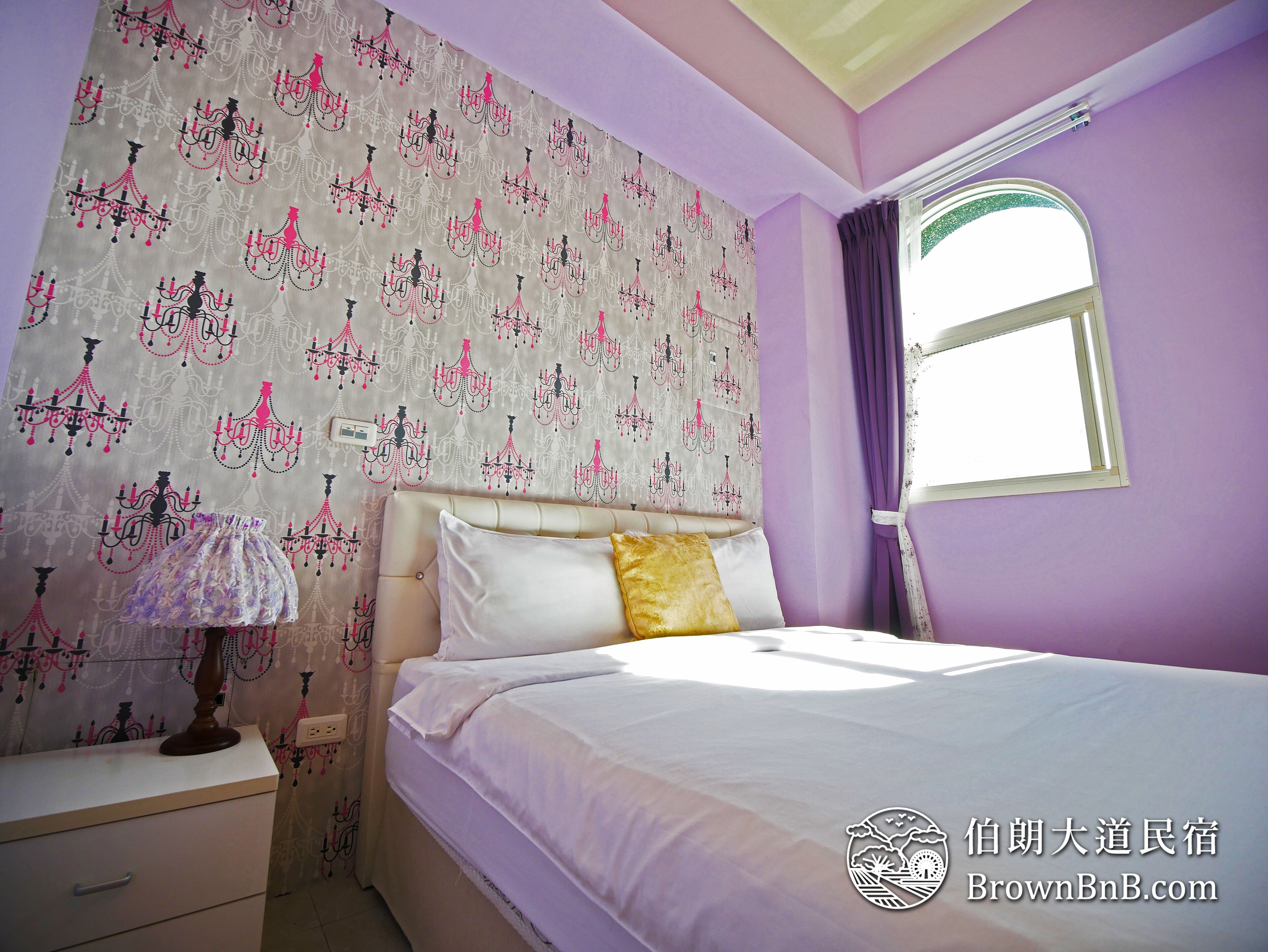 Un dormitorio con cama, mesita de noche, lámpara y ventana con cortinas.
