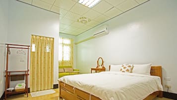 Un dormitorio con cama, mesita de noche con espejo, perchero y ventana con cortinas.