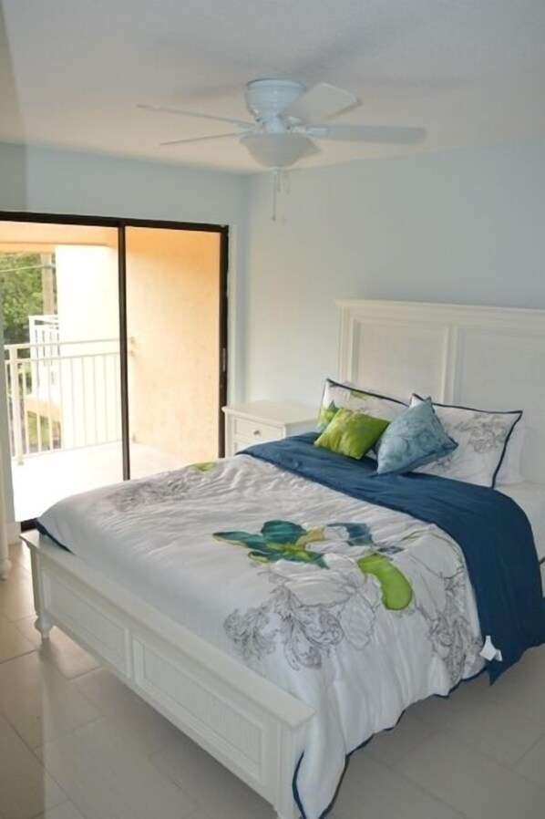 A bedroom with a bed, a ceiling fan, a nightstand, and a view of the outside.