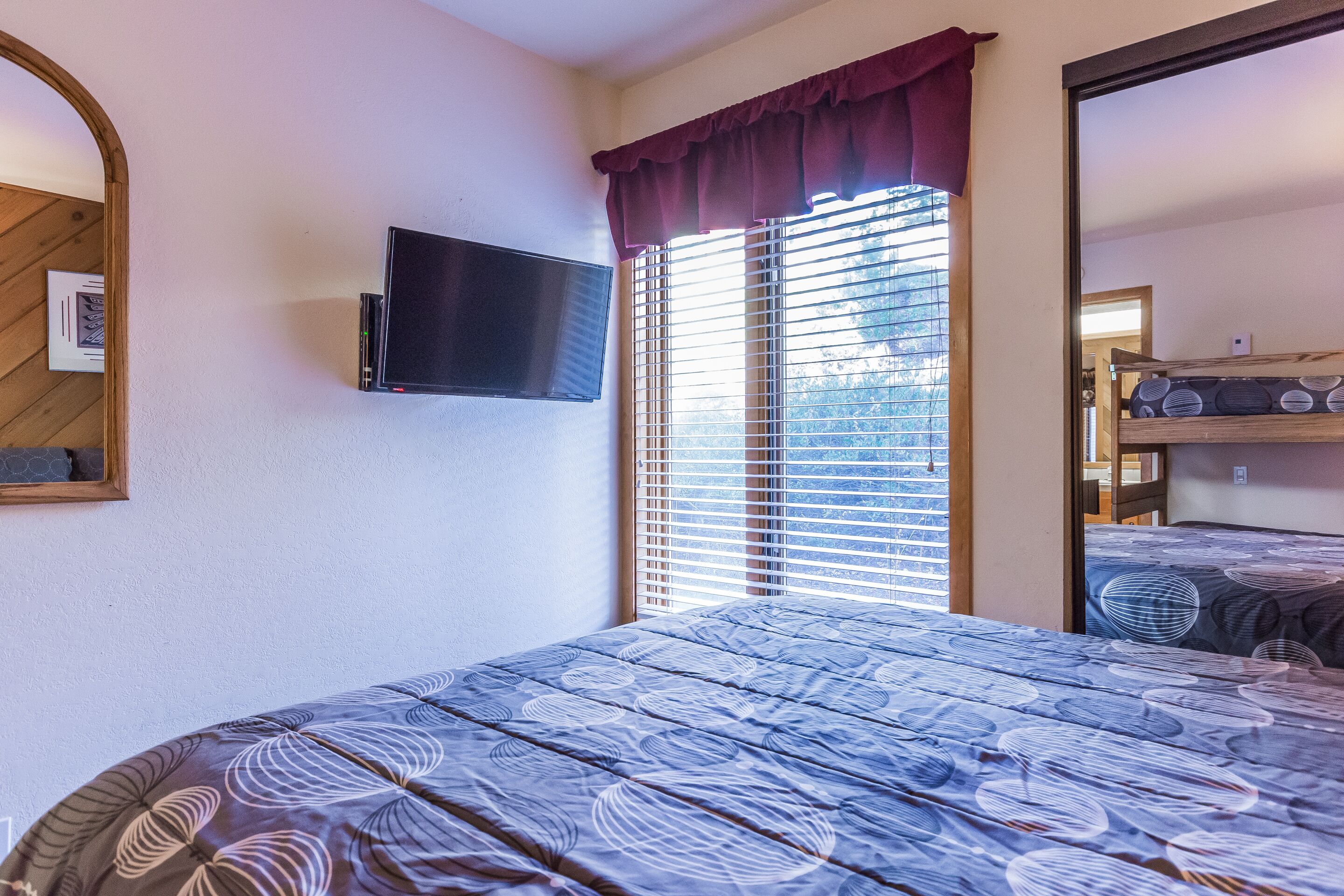 Une chambre à coucher avec un lit, un téléviseur fixé au mur et une fenêtre avec des stores.