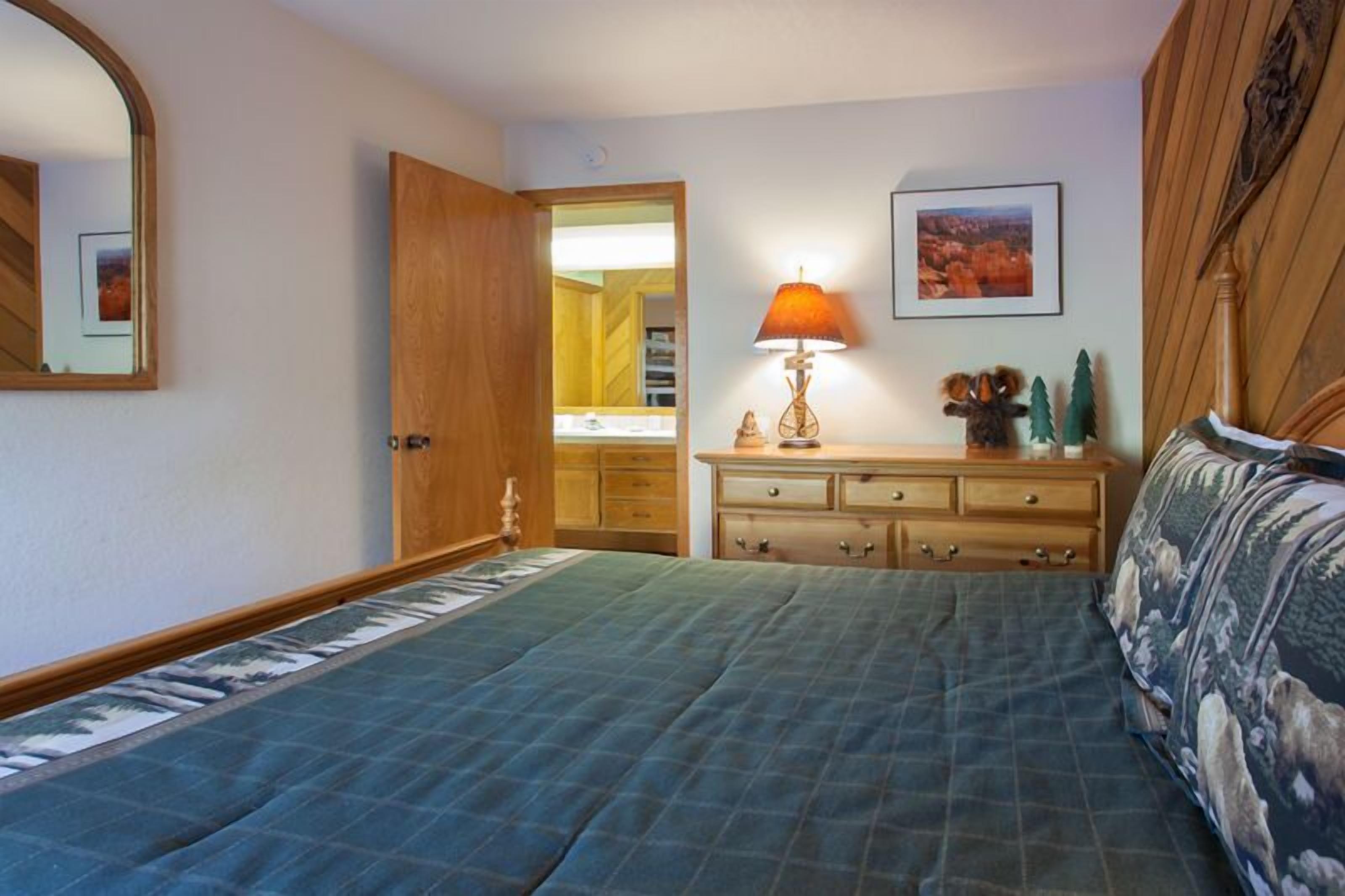 A bedroom with a bed, a dresser, a mirror, a lamp, and a framed picture on the wall.