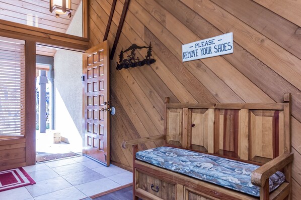 Interior d'una cabana de fusta amb una cadira, un cartell que indica treure els calçats i vista cap a l'exterior.