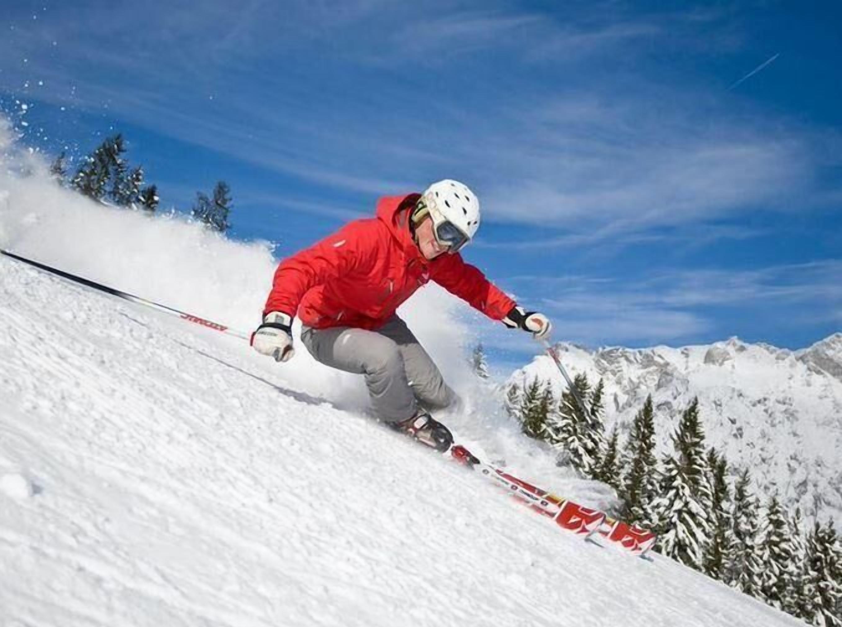 Une personne fait du ski sur une pente enneigée, avec un ciel bleu dégagé en arrière-plan.