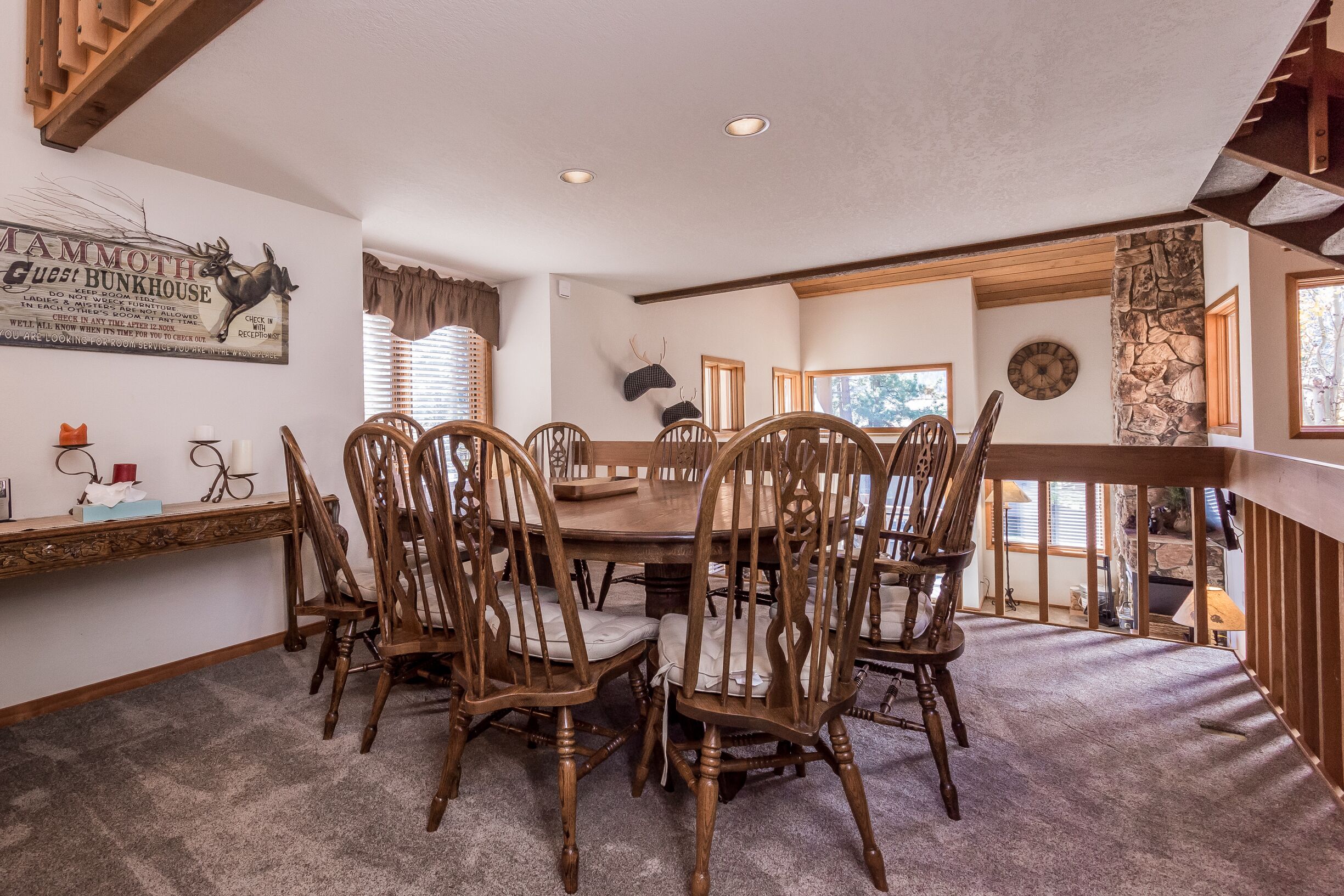 A dining area with a wooden table and chairs, a wall clock, and a sign with a deer and antlers.