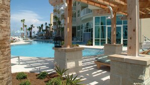 A pool area with lounge chairs and umbrellas, surrounded by palm trees and a multi-story building with balconies. - Stunning 11th Floor Gulf-View Retreat at Aqua Resort Free Beach Chairs (Panama City Beach)