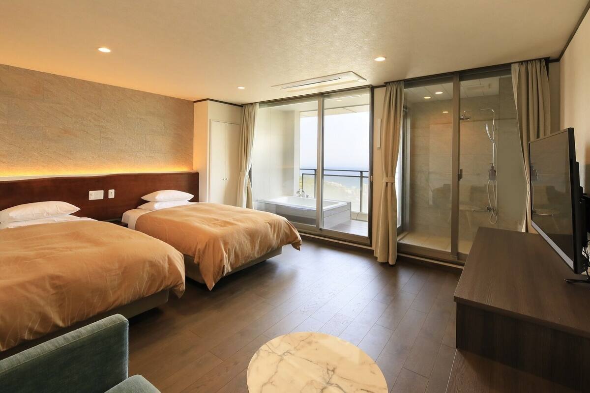 A hotel room with two beds, a TV, a desk, and a balcony with a glass door.
