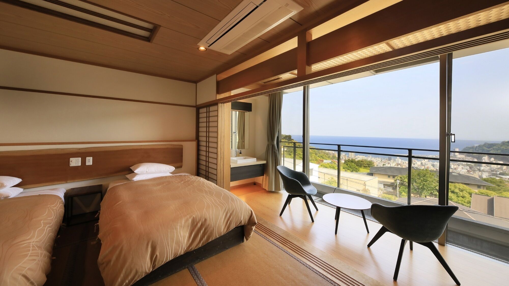 Een hotelkamer met twee bedden, een balkon en uitzicht, plus een tafeltje met stoelen.