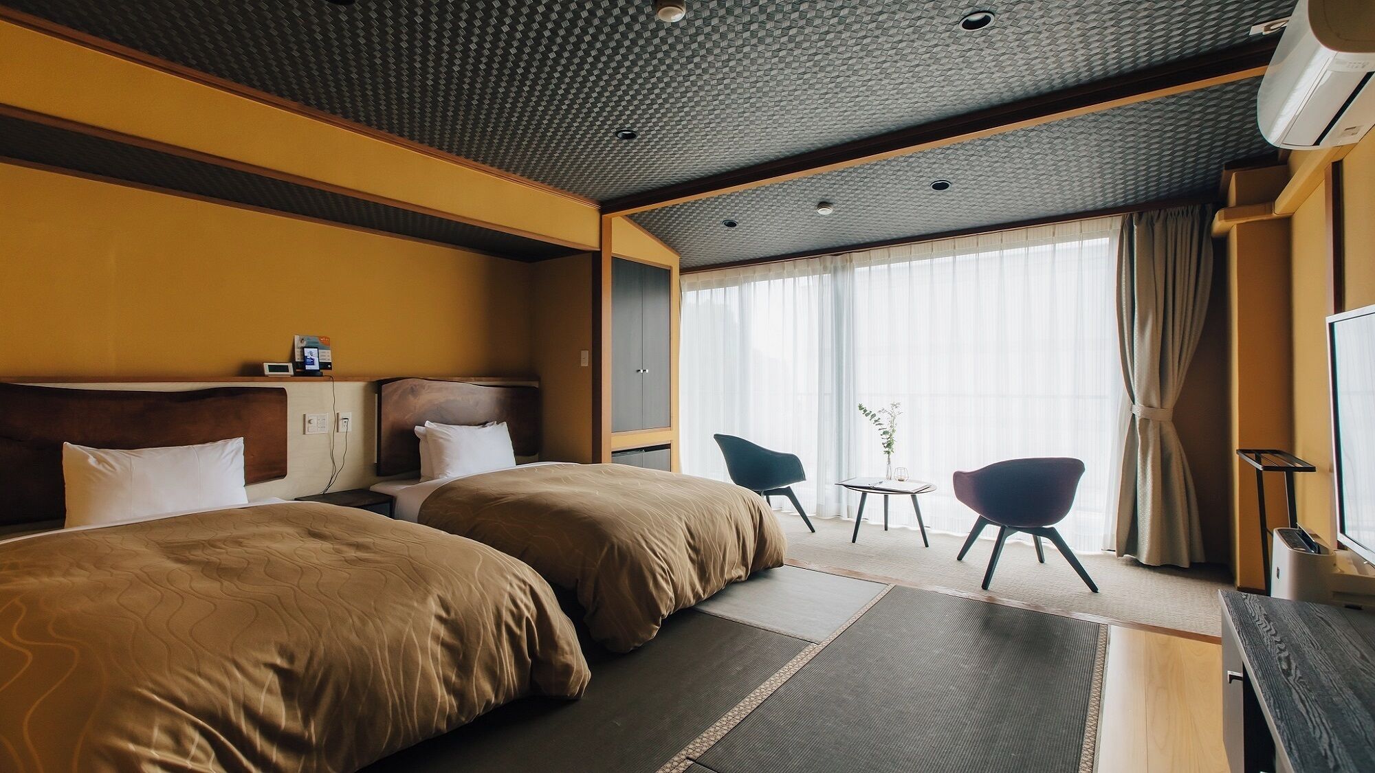 Een hotelkamer met twee bedden, een bureau, een stoel, een televisie en een groot raam met gordijnen.