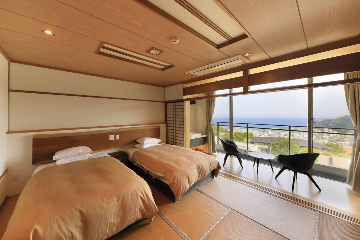 A hotel room with two beds, a balcony with a view, and a seating area.