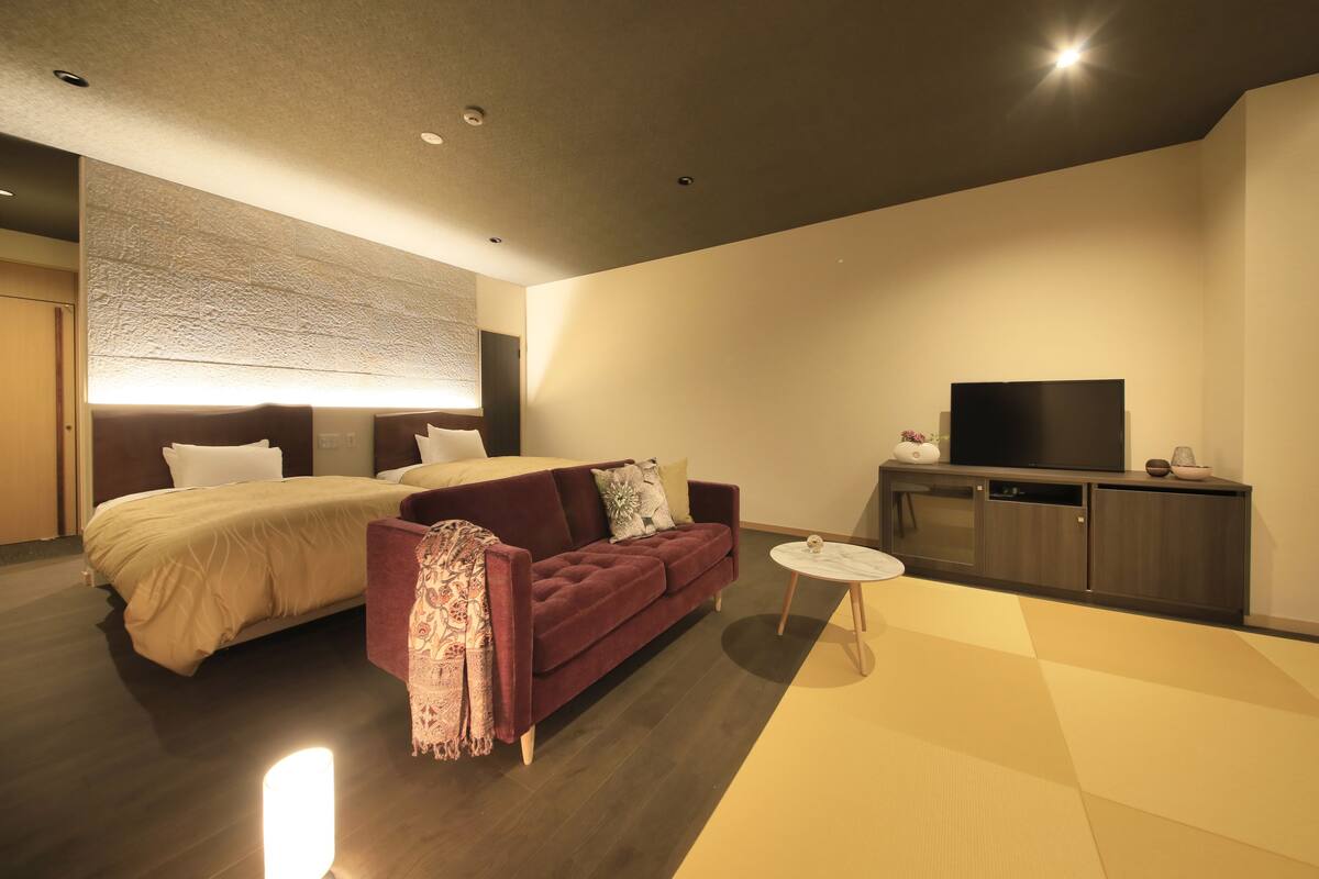 A modern hotel room with a large bed, a red sofa, a small round coffee table, a TV, and a cabinet.