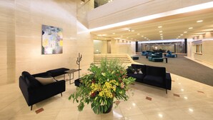 A spacious lobby with modern black sofas, a large floral arrangement, and a high ceiling with recessed lighting. - Atami Fuga (Atami)