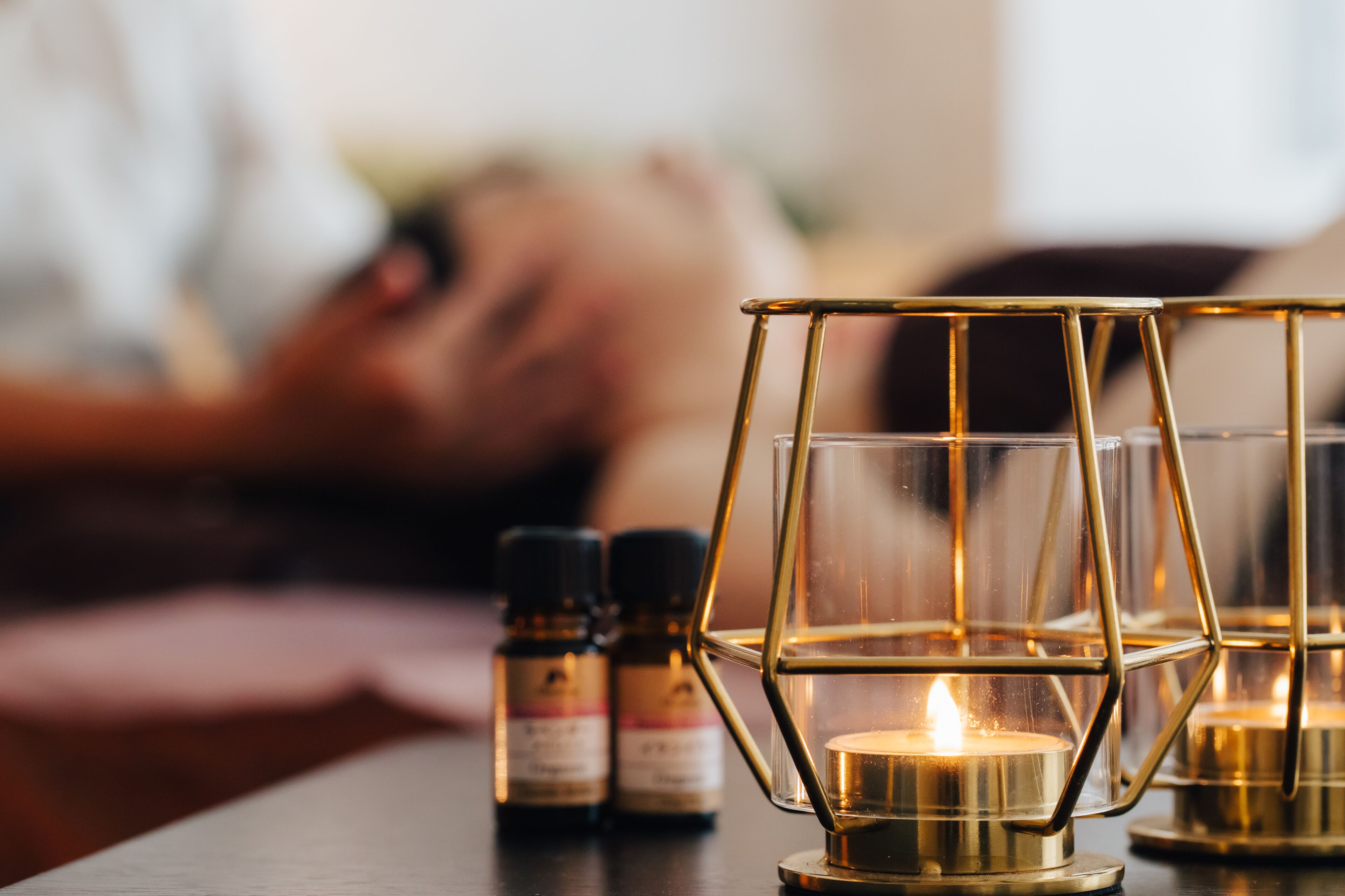 A candle holder with a lit candle, a bottle of essential oil, and a blurred background.