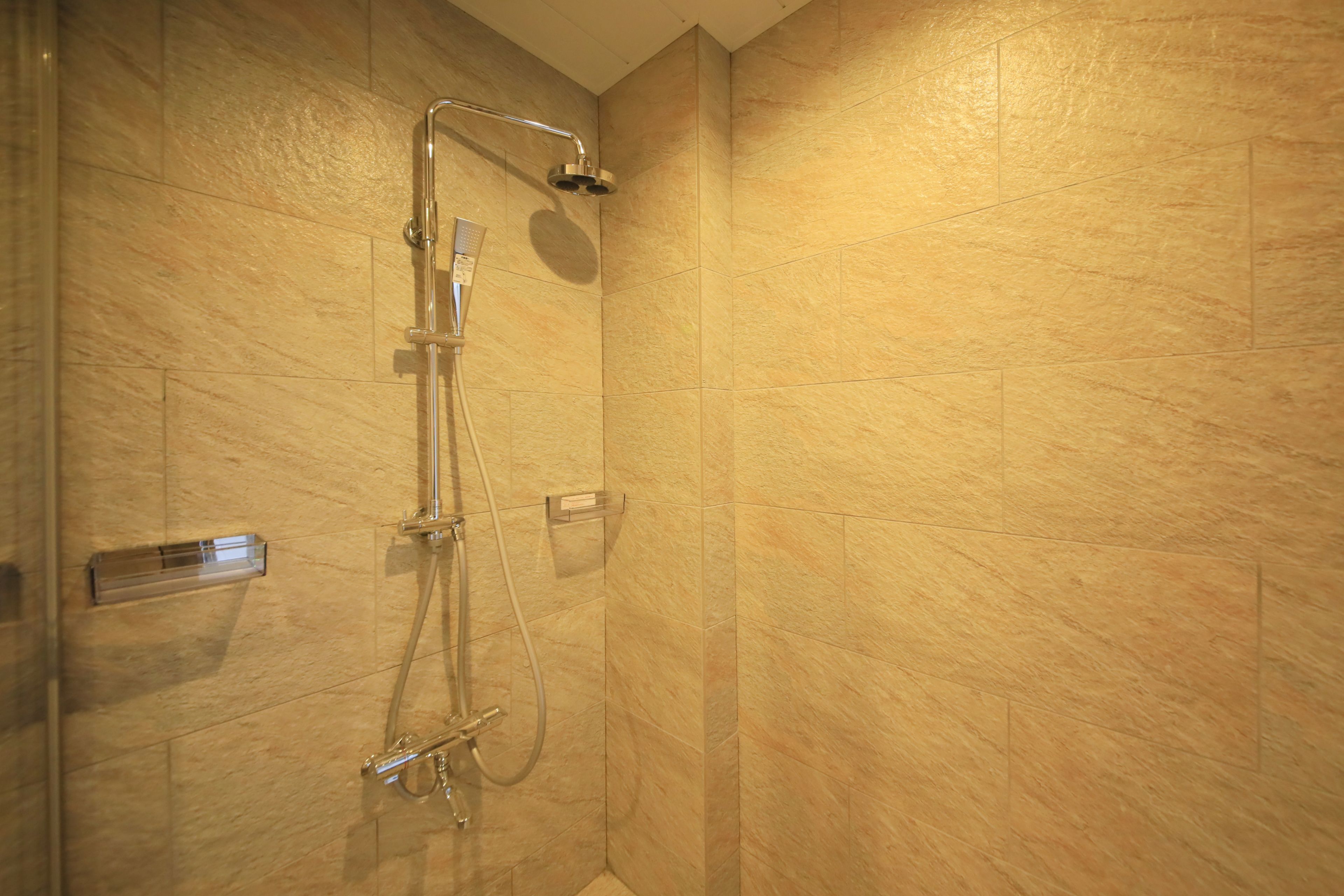 A shower with a handheld showerhead and a wall-mounted control panel.