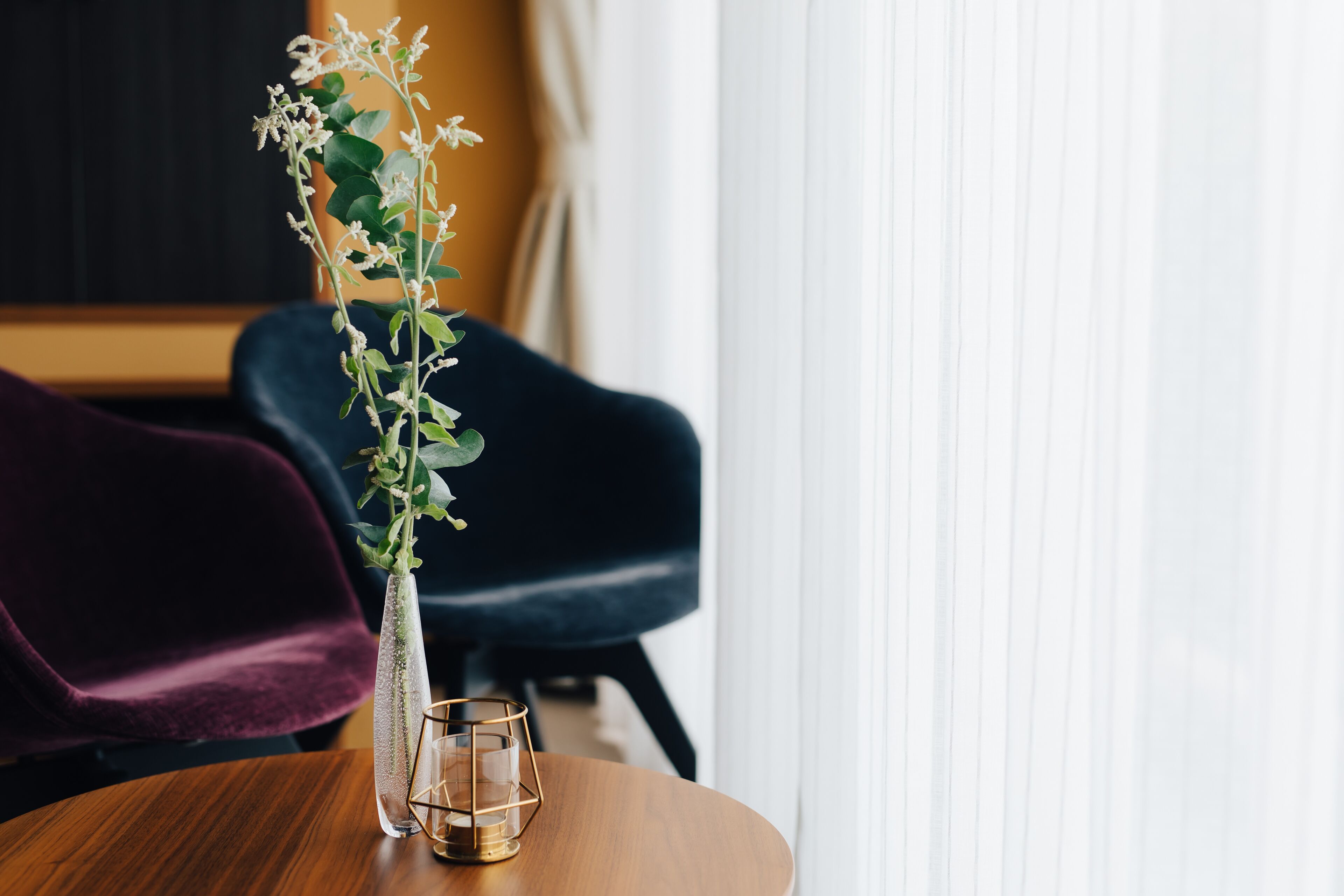 A wooden table with a clear glass vase containing a plant and a candle.