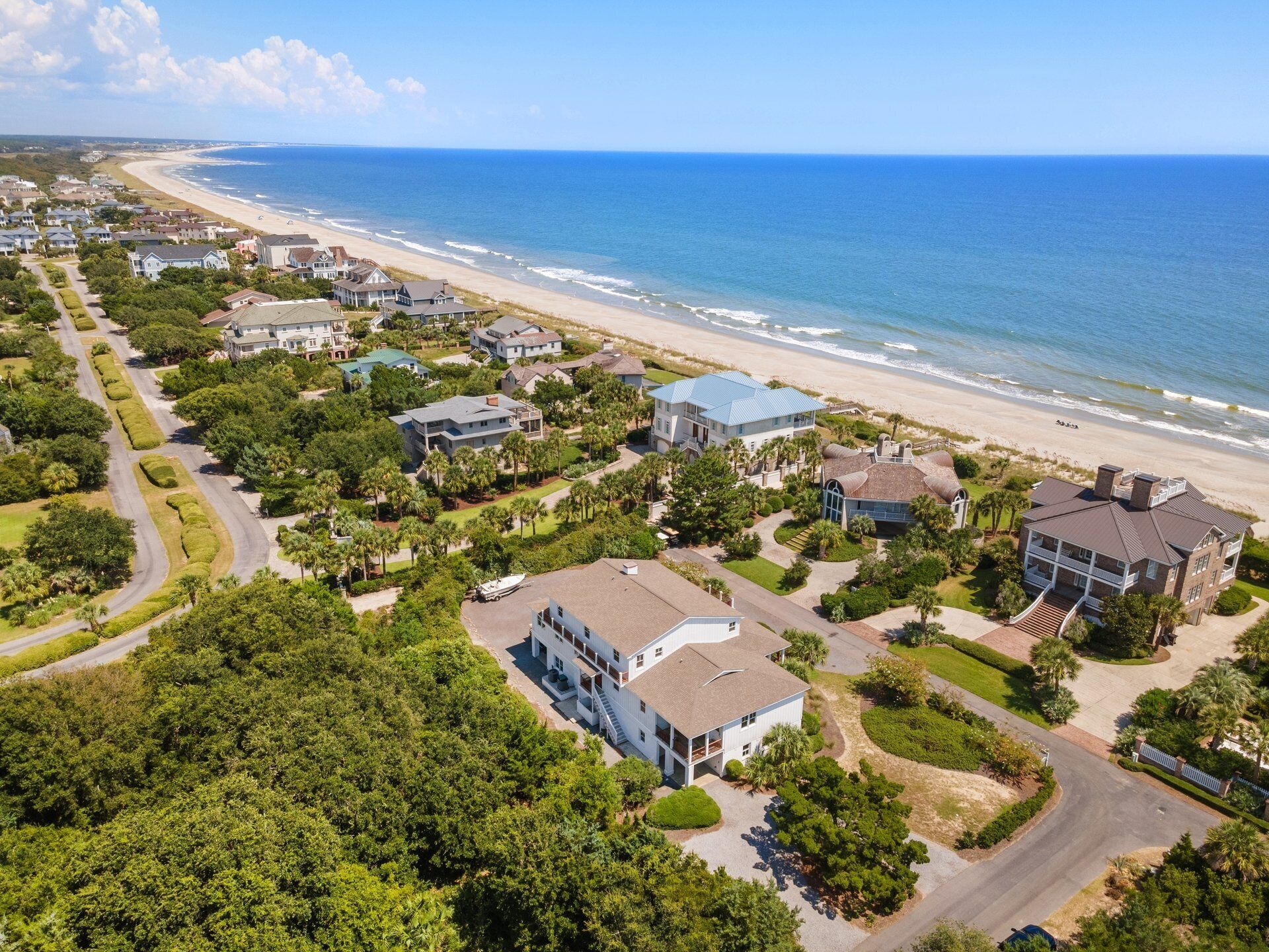 Vue aérienne d’une zone résidentielle côtière, avec des maisons, une plage et un ciel dégagé.
