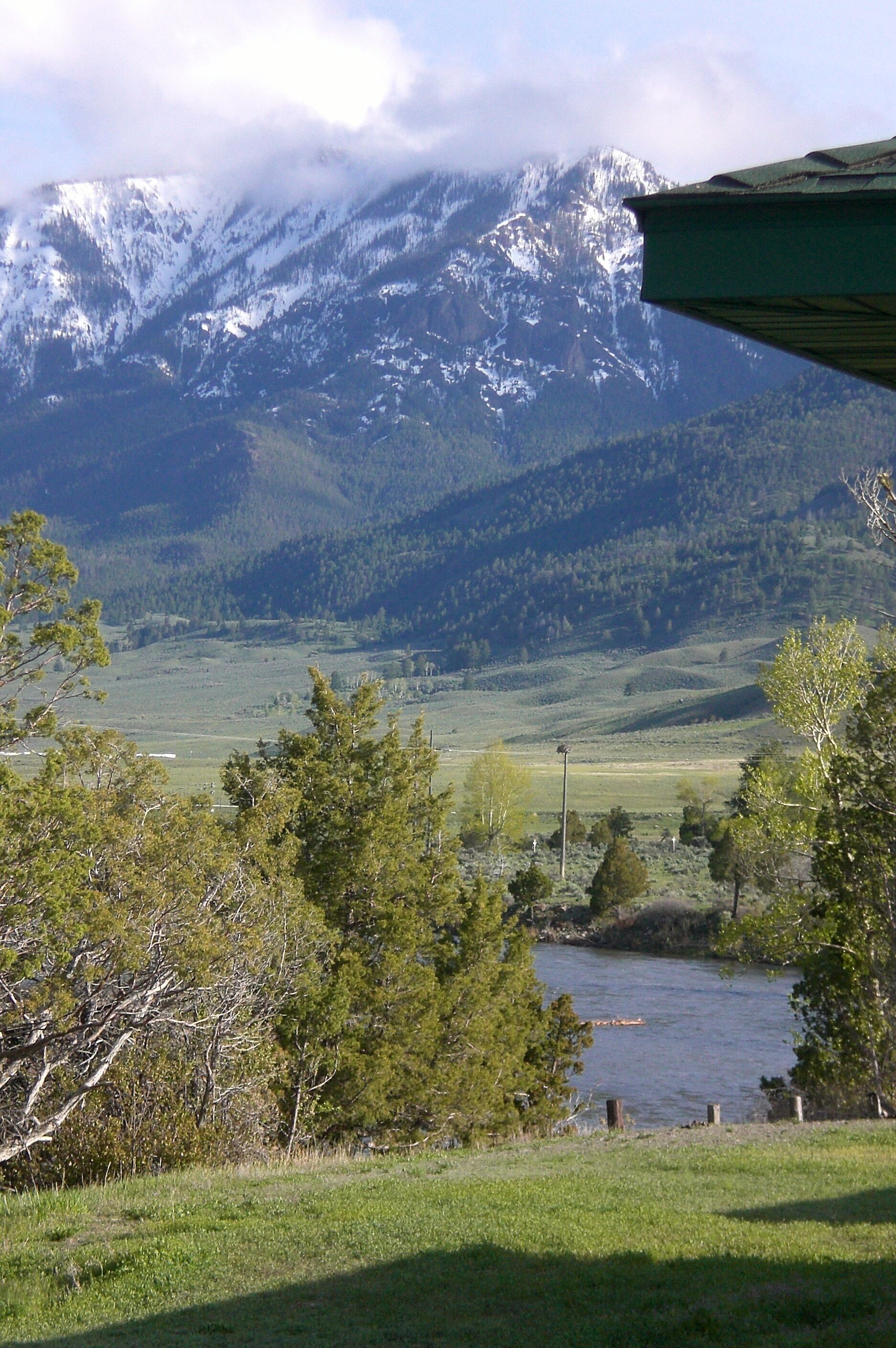 Un paysage montagneux avec des sommets enneigés, une rivière et un champ verdoyant.