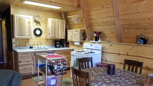 A cozy cabin-style kitchen with wooden walls, a dining table with chairs, a coffee maker, and a stove.
