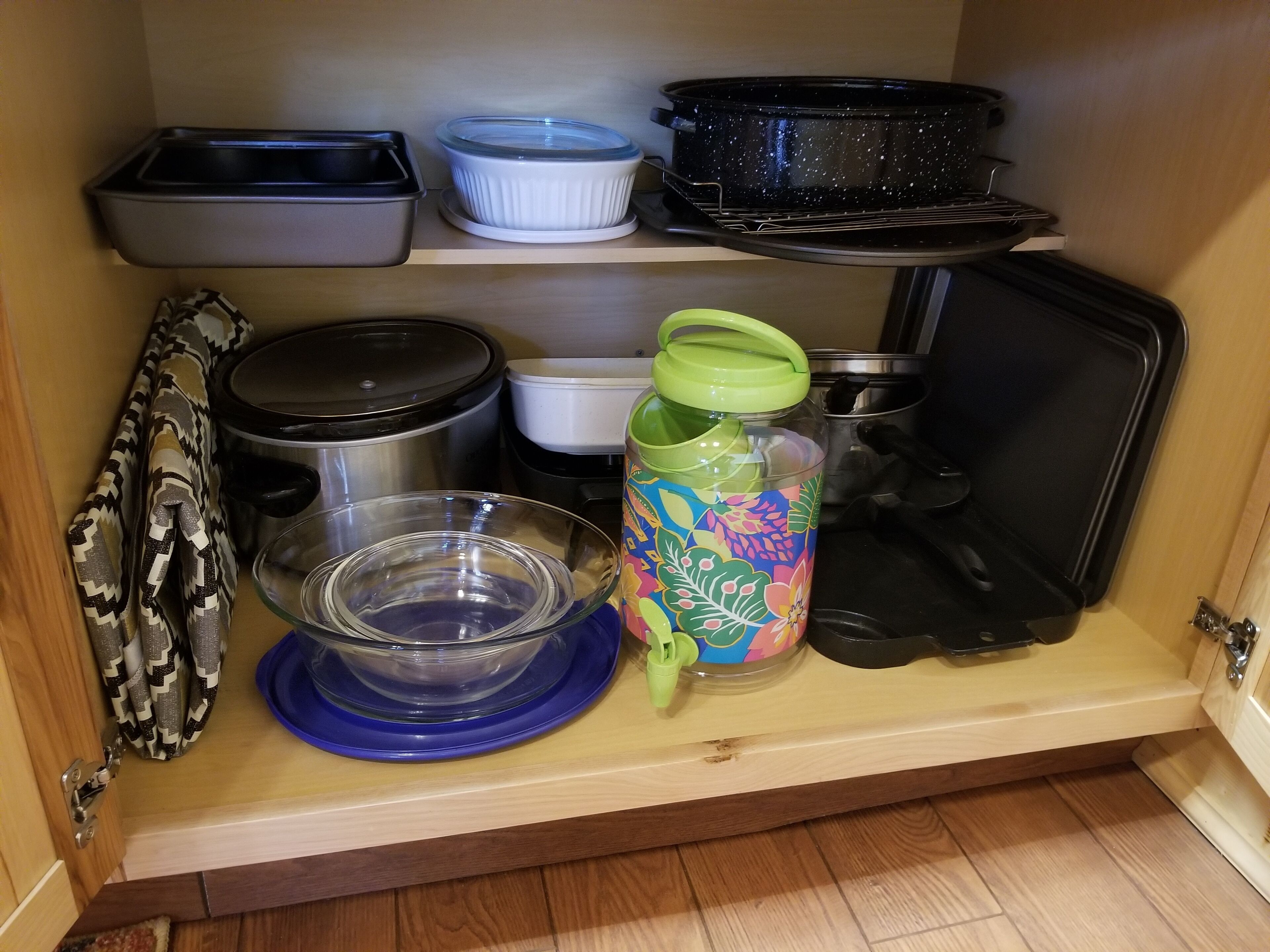A kitchen cabinet with various containers, including a blue bowl, a colorful water bottle, and several pots and pans.