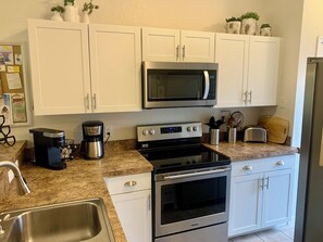 A modern kitchen with white cabinets, a built-in microwave, a stove, a coffee maker, and a toaster.