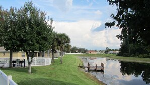 A grassy area with a dock extending into a calm body of water, surrounded by trees and a white fence. - Gem of Lake Marion! Beautiful 3 Bedroom with King Beds, HD & Internet (Kissimmee)