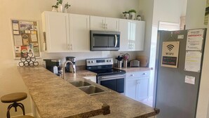 A kitchen with white cabinets, a microwave, a stove, and a sink. There are two stools and a refrigerator with a WiFi sign. - Gem of Lake Marion! Beautiful 3 Bedroom with King Beds, HD & Internet (Kissimmee)