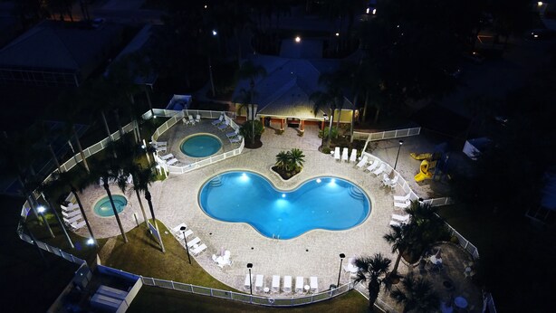 A large outdoor swimming pool area with multiple pools, surrounded by white lounge chairs and umbrellas, and a fenced walkway. - Gem of Lake Marion! Beautiful 3 Bedroom with King Beds, HD & Internet (Kissimmee)