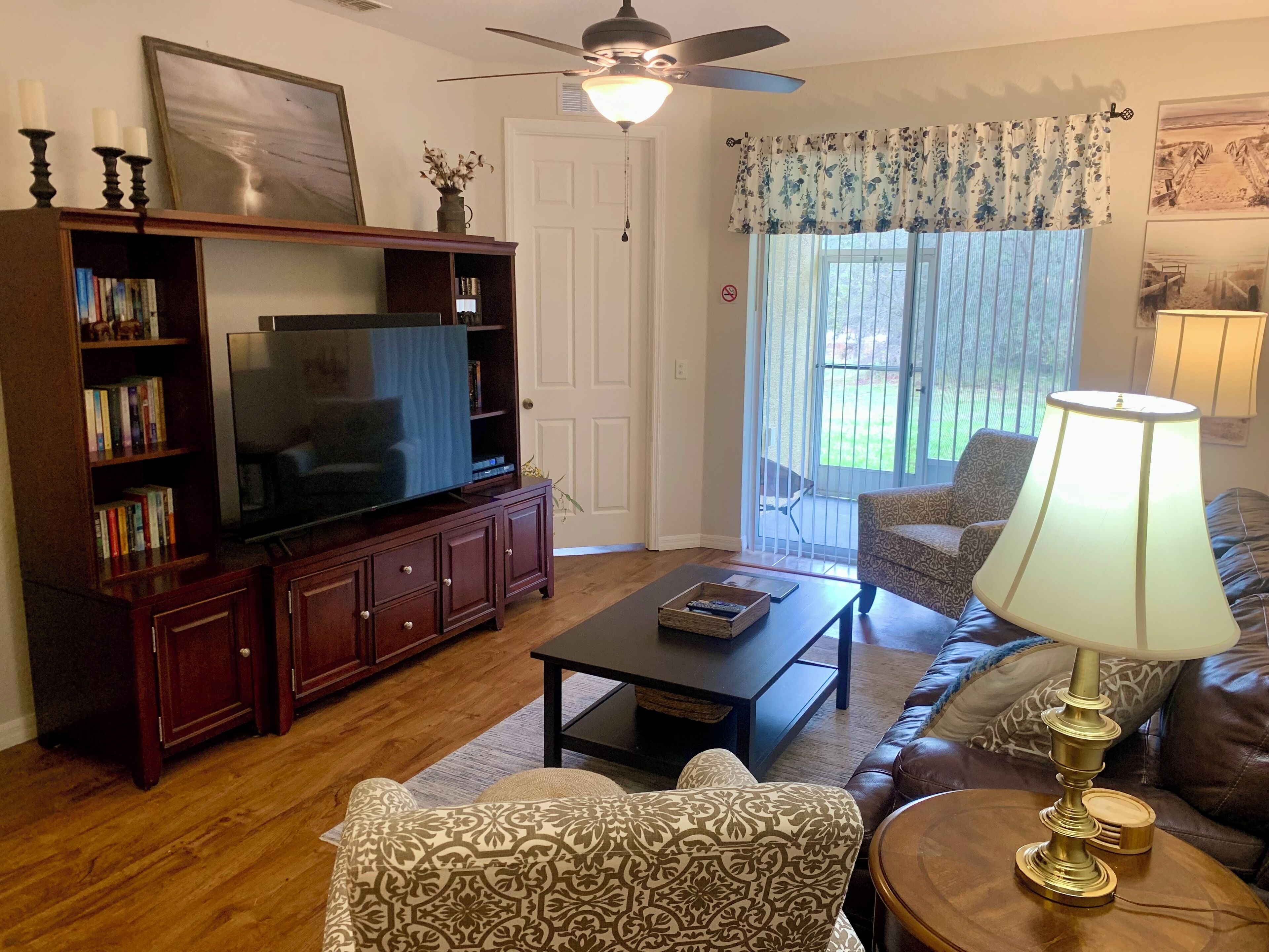 Una sala de estar con televisión, estantería, sillón estampado, mesa de centro y lámpara.