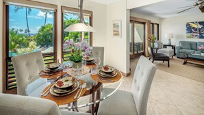 Un comedor con mesa de vidrio, sillas y vista al océano. Hay un sofá y un cuadro en la sala.