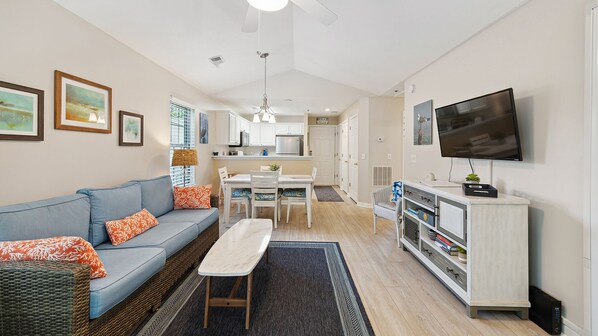 A compact living space with a sofa, dining table, kitchen area, and a TV mounted on the wall.