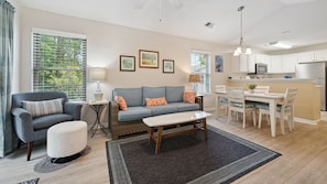 A living room with a sofa, armchair, and coffee table, a dining area with a table and chairs, and a kitchen with a refrigerator and microwave.