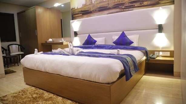 Una habitación de hotel con una cama grande, dos mesitas de noche, una silla y una lámpara de pared.