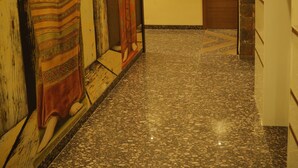 Un pasillo con suelo de mármol, una puerta de madera y dos estatuas adosadas a la pared.